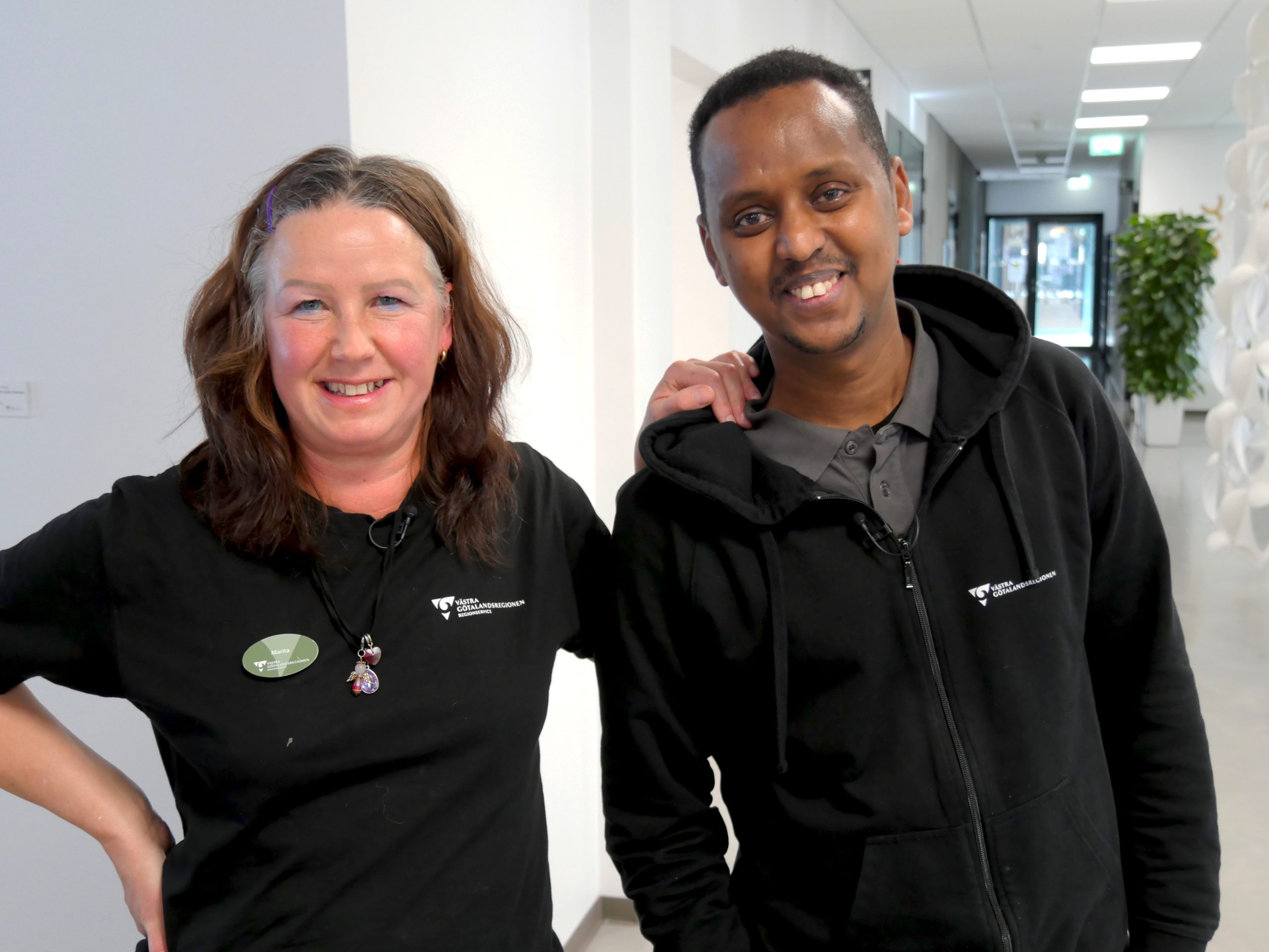 Servicepersonalarbetarna Marita och Abdi som håller om varandra glada och i arbetskläder